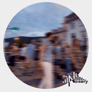 City street ambience sound effects library image on Sonniss: dusk, people blurred, buildings, green traffic light, Noisery logo.