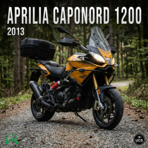 Orange 2013 Aprilia Caponord 1200 adventure touring motorbike with rear luggage case parked on a forest gravel track.