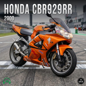 Orange 2000 Honda CBR929RR sport bike parked on a racetrack starting grid.