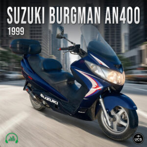 Blue 1999 Suzuki Burgman AN400 maxi touring scooter with tall windshield and rear storage case drives along city street.