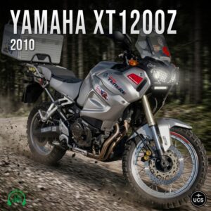 Silver 2010 Yamaha XT1200Z adventure touring motorbike with a rear luggage case rides along a forest dirt track.